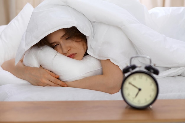 Hermosa joven durmiendo en la cama y relajándose por la mañana. Un día soleado empieza es el momento de ir a trabajar o dormir los fines de semana.