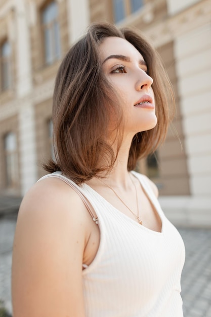 Hermosa joven elegante con una cara linda y un corte de pelo corto con un vestido blanco elegante caminando afuera en un cálido día de verano