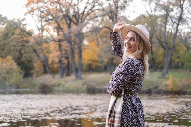 Hermosa joven elegante con sombrero camina en la naturaleza en el parque de otoño en otoño.