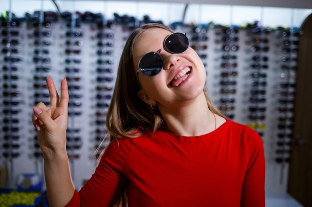 Hermosa joven elige gafas de sol en una tienda de óptica.