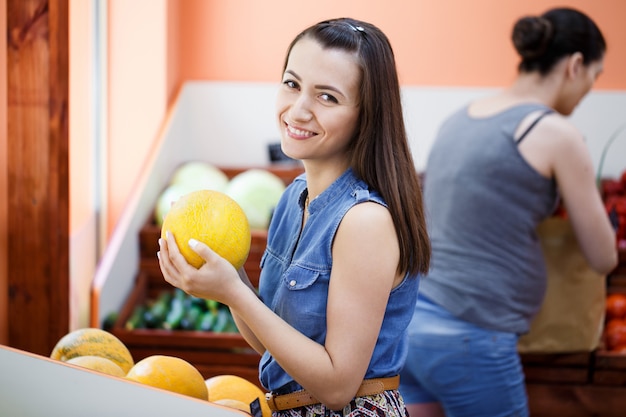 Hermosa joven elige melones en una tienda de verduras