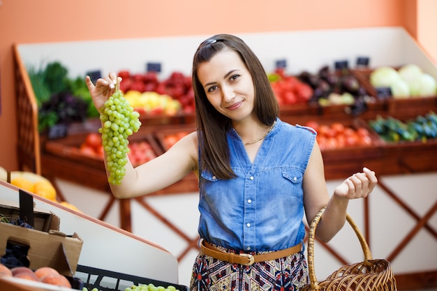 Hermosa joven elige uvas en una tienda de verduras