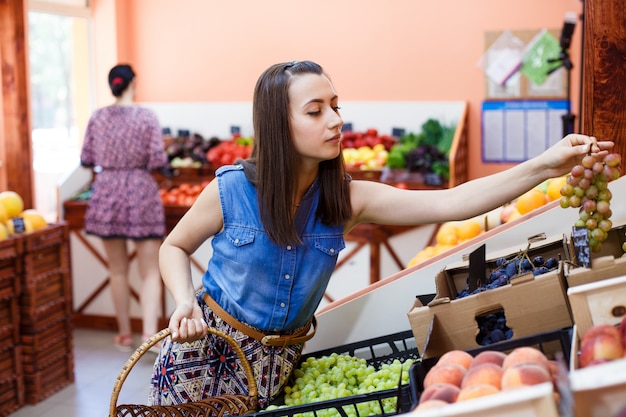 Hermosa joven elige uvas en una tienda de verduras