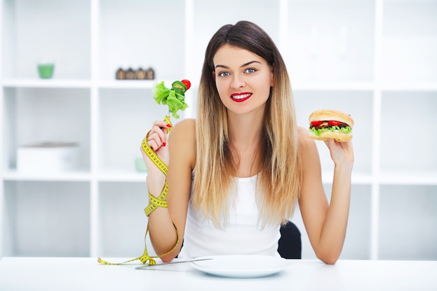 Hermosa joven eligiendo entre comida sana y comida chatarra