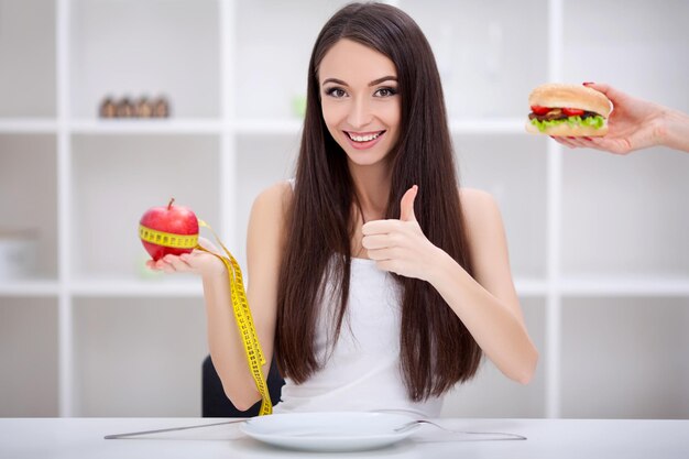 Hermosa joven eligiendo entre frutas y comida chatarra