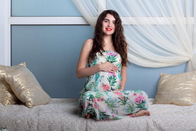 Hermosa joven embarazada con cabello rizado en un vestido largo