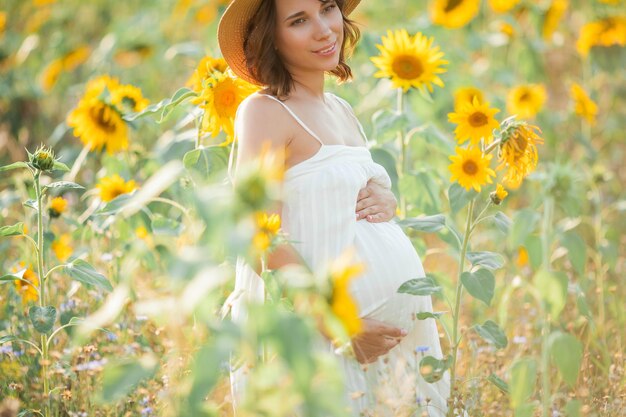 Hermosa joven embarazada en el campo de girasol. Retrato de una joven embarazada al sol. El verano.