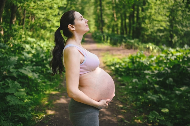 Hermosa joven embarazada con gran barriga posando en el parque de verano al aire libre