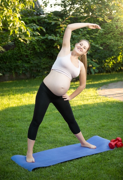 Hermosa joven embarazada haciendo ejercicio sobre la hierba verde en el parque