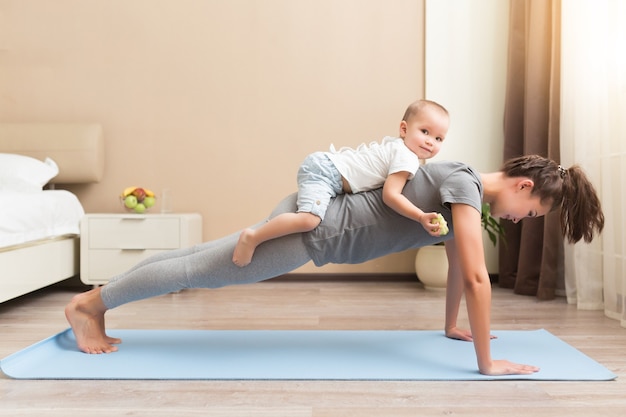 Hermosa joven embarazada y niño pequeño sonriendo mientras está acostado en la estera de yoga