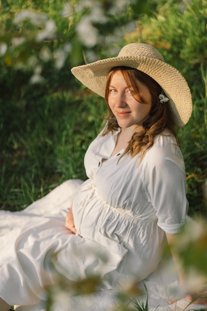 Una hermosa joven embarazada con un vestido blanco en el jardín de primavera