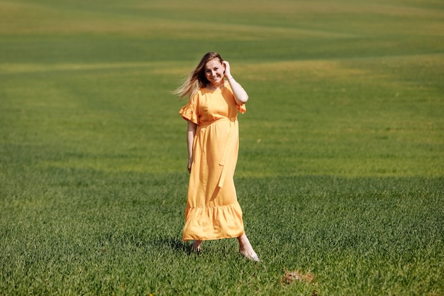 Foto hermosa joven embarazada en vestido largo en el campo verde el día de verano.