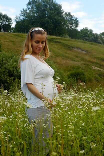 Hermosa joven embarazada con el vientre desnudo camina en flores silvestres en la pradera. Embarazo en la naturaleza del color, ella está en su séptimo.