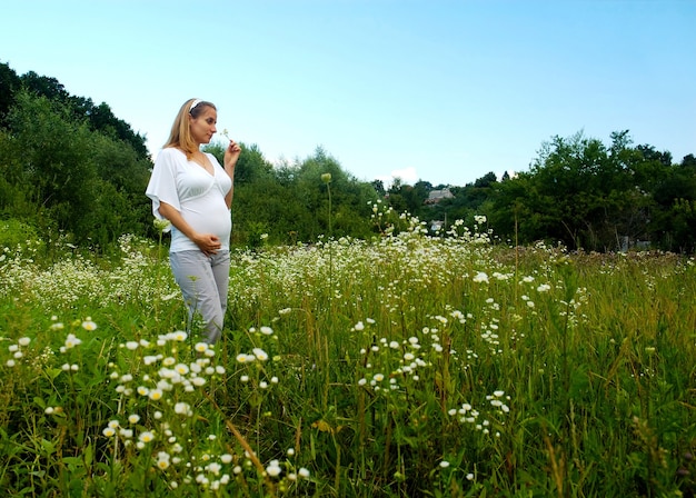 Hermosa joven embarazada con el vientre desnudo camina en flores silvestres en la pradera.