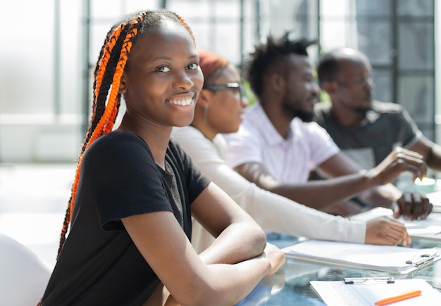 Hermosa joven empresaria africana con colegas en el fondo