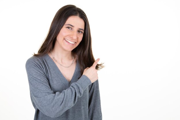 Hermosa joven empresaria apuntando con el dedo y mirando a la cámara con una sonrisa de pie contra el fondo blanco.