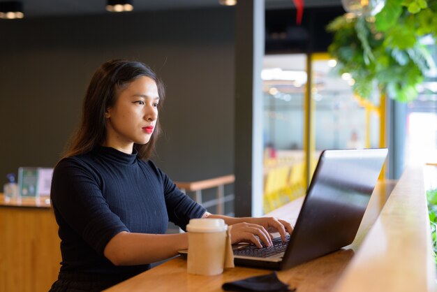 Hermosa joven empresaria asiática usando laptop y sentado con distancia dentro de la cafetería