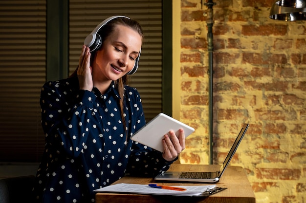 Hermosa joven empresaria con auriculares está sentada en una tableta de oficina colocada en la oficina