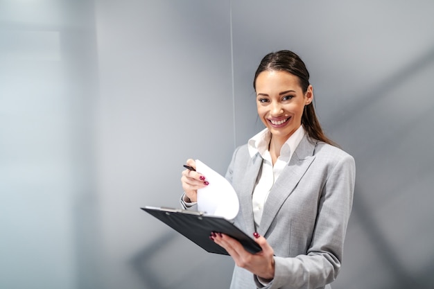 Hermosa joven empresaria caucásica positiva sonriente de pie dentro de la firma corporativa y firma de contratos.