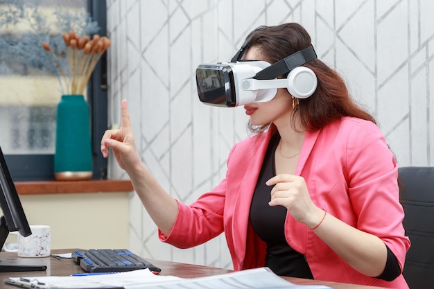 Hermosa joven empresaria con gafas VR y pinta su dedo en la PC Foto de alta calidad