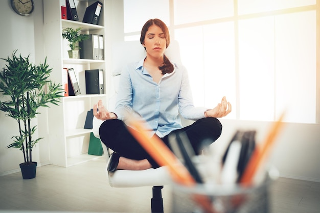 Hermosa joven empresaria sentada en posición de loto mientras meditaba en la oficina.