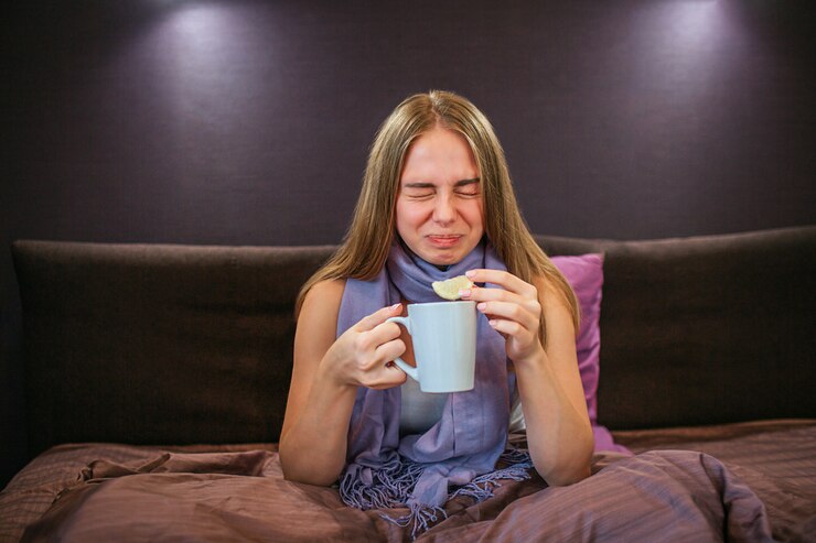 Foto hermosa joven se encoge de limón agrio. ella sostiene un pedazo en una mano y una taza de té caliente en otra. la mujer sufre.