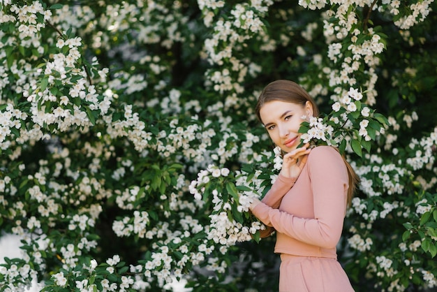 Una hermosa joven se encuentra junto a un manzano blanco floreciente decorativo en primavera