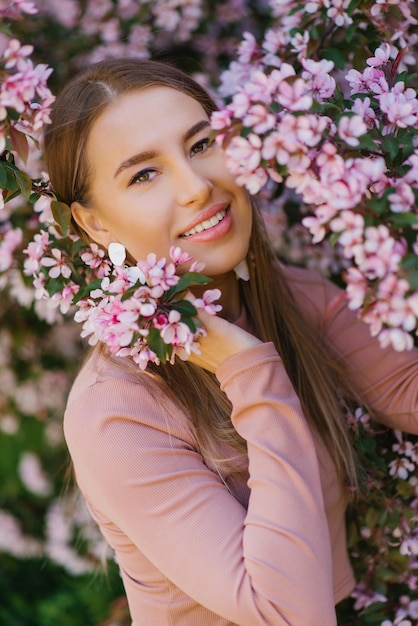 Una hermosa joven se encuentra junto a un manzano rosa floreciente decorativo en primavera