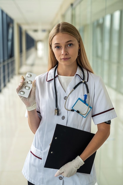 Hermosa joven enfermera se encuentra en el pasillo con un estetoscopio y una tableta Concepto de medicina