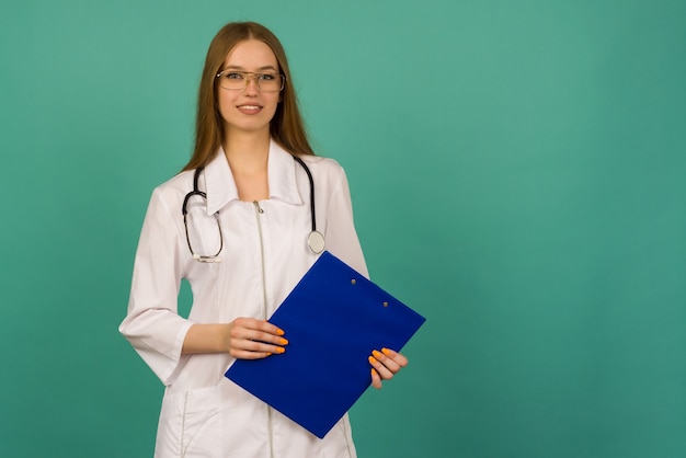 Hermosa joven enfermera o médico en formación con carpeta azul y estatoscopio en un espacio azul