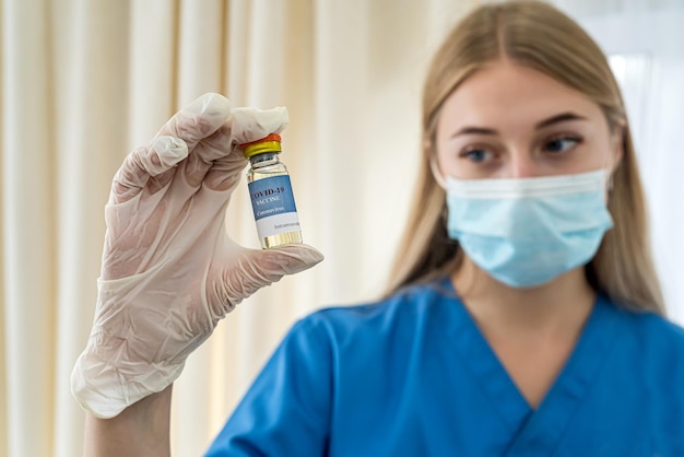 Hermosa joven enfermera en uniforme y guantes sosteniendo una vacuna Concepto de medicina Concepto de vacunación Concepto de covid