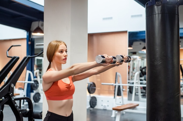 Hermosa joven entrena deltoides en el gimnasio con mancuerna