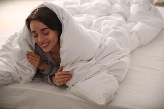 Hermosa joven envuelta con una manta suave relajándose en la cama en casa