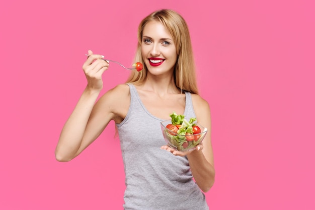 Foto hermosa joven esbelta con un fondo rosa comiendo una ensalada de verduras concepto de comida saludable