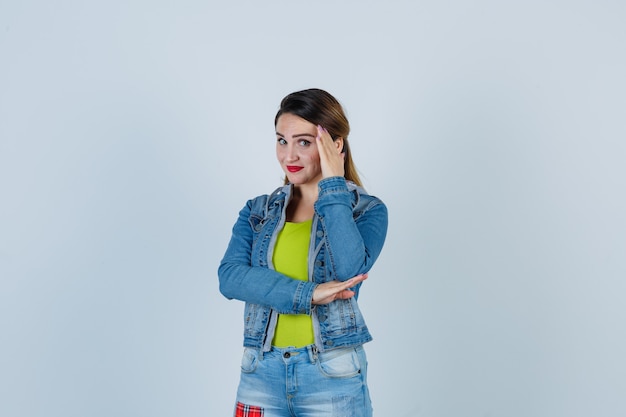 Hermosa joven escondiendo la cara detrás de la mano en traje de mezclilla y mirando avergonzado. vista frontal.