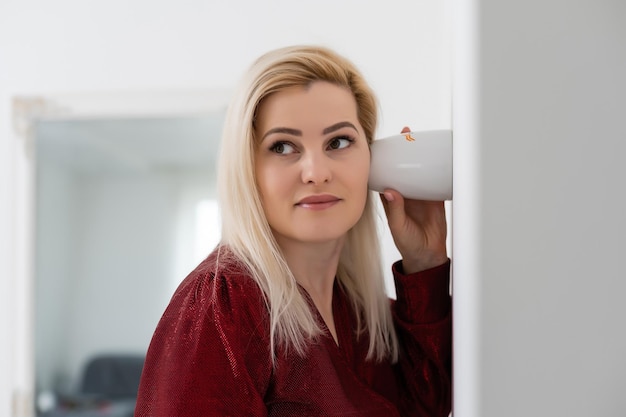 Hermosa joven escuchando a escondidas cerca de la pared usando una taza de té.