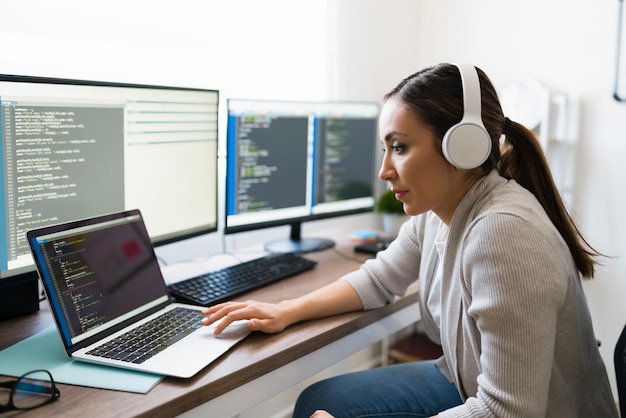 Hermosa joven escuchando música con auriculares mientras escribe código en su laptop. Programador disfrutando de su trabajo en casa