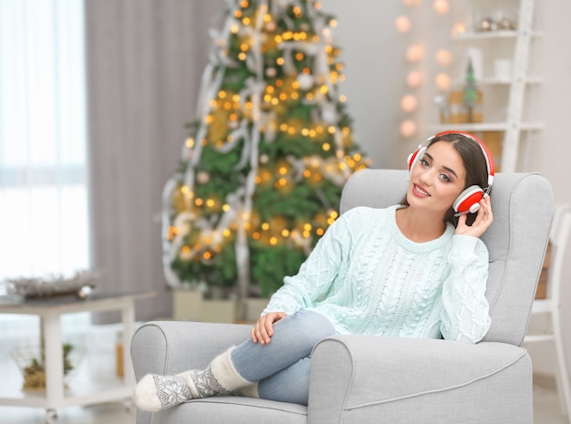 Hermosa joven escuchando música en el salón decorado para Navidad