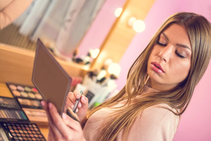 Foto una hermosa joven en el espejo aplicando maquillaje