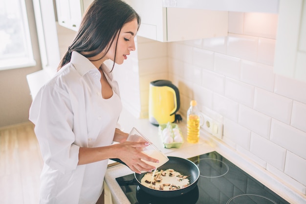 Hermosa joven está cocinando el desayuno.