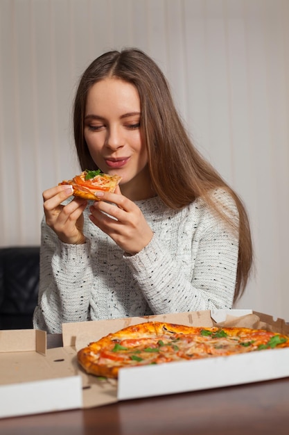 Hermosa joven está comiendo pizza en la oficina