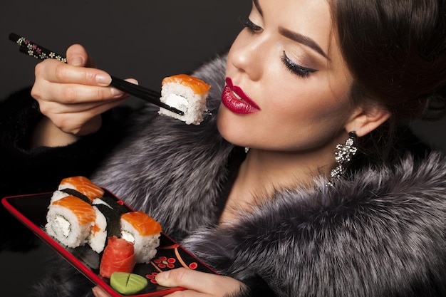 Hermosa joven está comiendo sushi sobre fondo negro