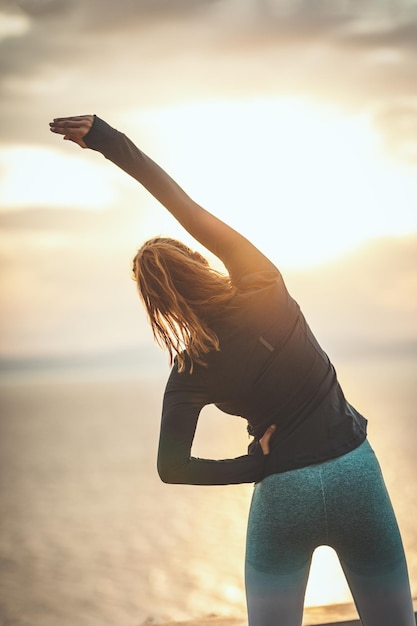 Una hermosa joven está haciendo ejercicio de estiramiento por los ses al amanecer.