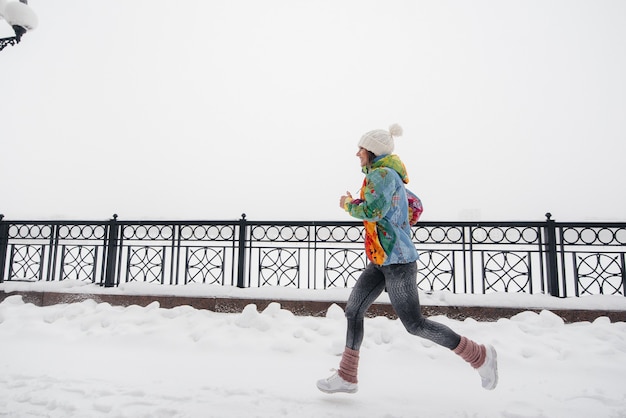 Una hermosa joven está haciendo jogging en un día helado y nevado. Deportes, estilo de vida saludable.