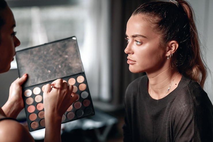 Foto hermosa joven está mirando al maquillador con una gran paleta colorida de sombras, industria de la moda