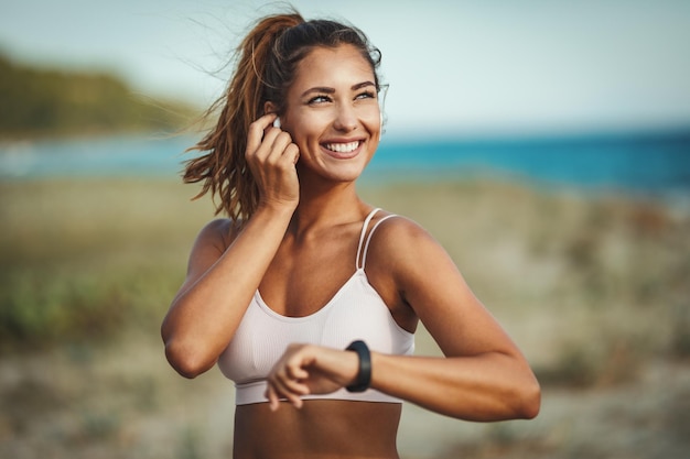 Una hermosa joven está mirando un reloj inteligente y preparándose para correr en la playa del mar en un día soleado de verano.