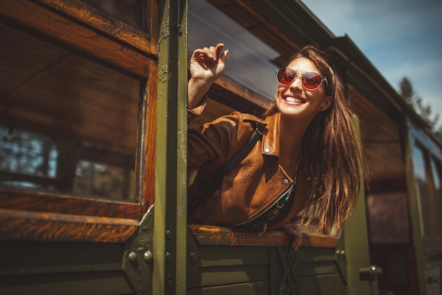 Una hermosa joven está mirando a través de una ventana de tren retro y está saludando a alguien durante su viaje a una aventura.