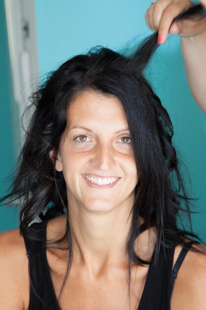 Hermosa joven se está peinando en el salón de belleza. Ella está sentada y sonriendo. La peluquera está tocando su cabello con cuidado.