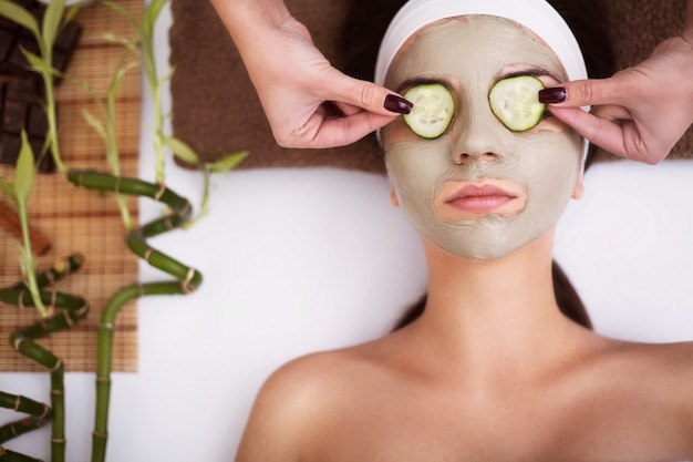 Hermosa joven está recibiendo máscara de arcilla facial en el spa