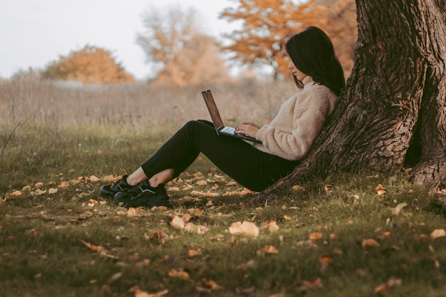 Hermosa joven está trabajando detrás de una computadora portátil en un parque de otoño